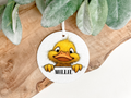 A baby duckling in cartoon style printed  onto a round soft air freshener both sides 8cm diameter  with a hanging ribbon and personalised with a name