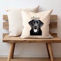 A cream cushion cover with a Black Labrador dog  printed on one side with a personalised name option, the cushion cover has a zip opening and is displayed on a small bench, the pet printing company